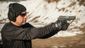 A man shoots a pistol with protective headphones and glasses on